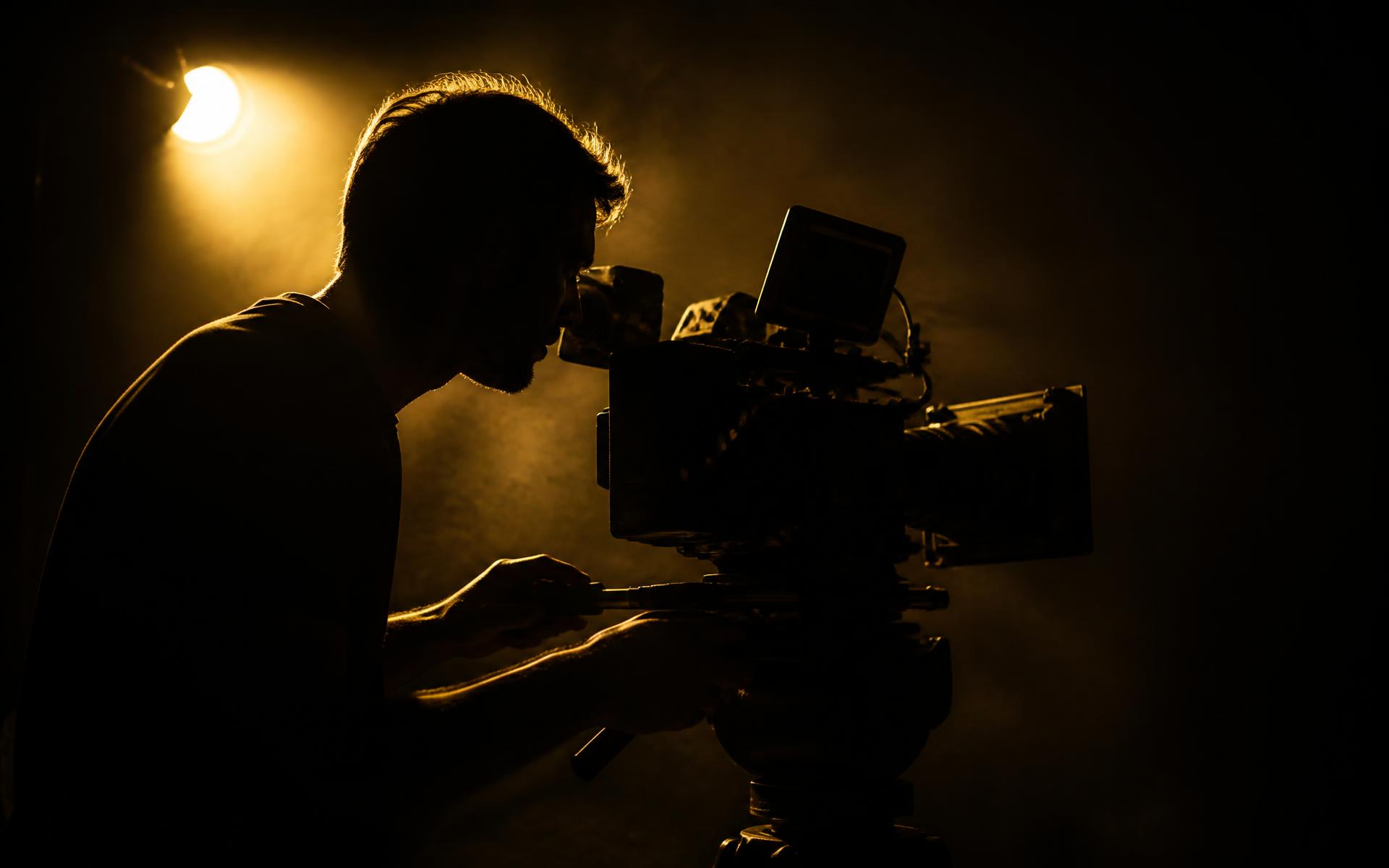 Cameraman filming in a dark studio lit with golden light